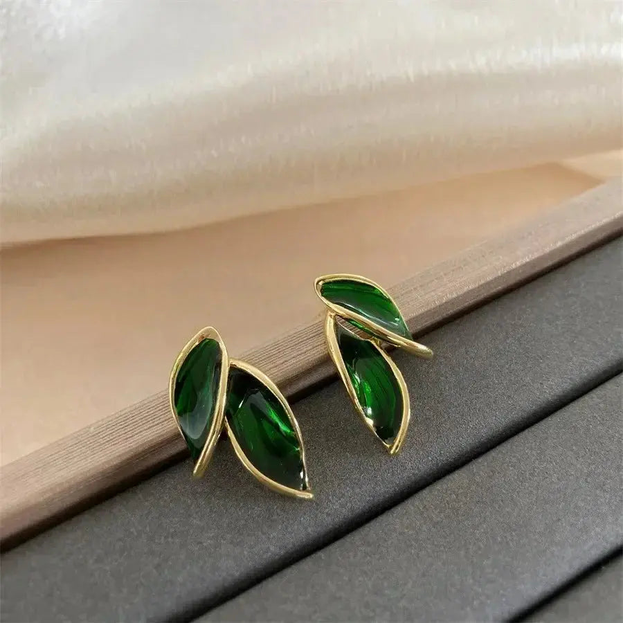 Green leaf-shaped earrings with gold accents on a textured surface