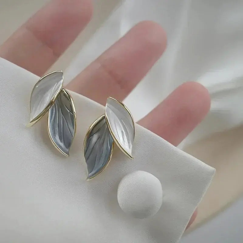 Pair of leaf-shaped earrings on a white cushion with a blurred background