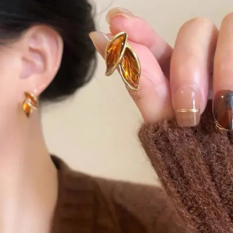 Close-up of a person wearing amber-colored leaf-shaped earrings.