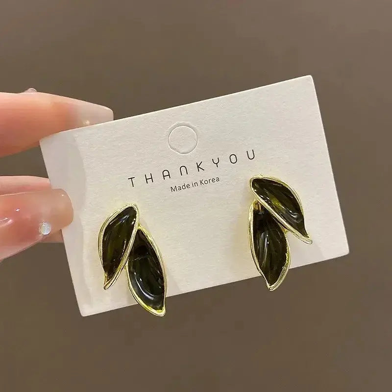 Pair of leaf-shaped earrings on a 'THANKYOU' branded card against a brown background