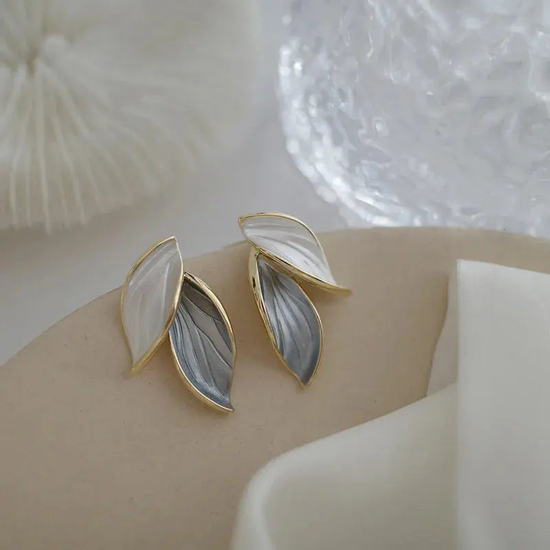 Gold and gray leaf-shaped earrings on a neutral background