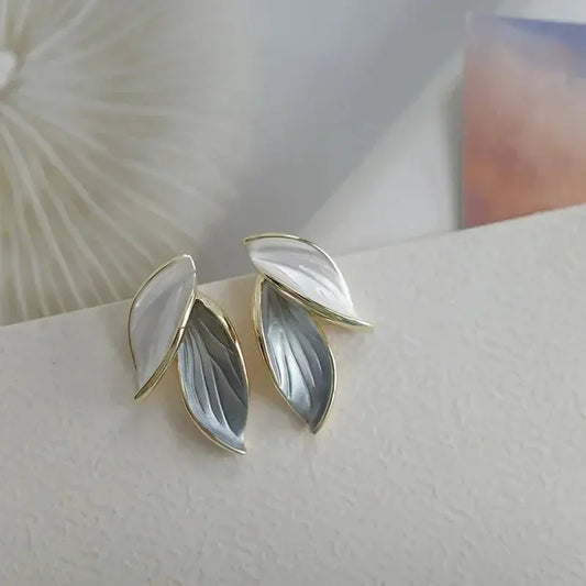 Pair of gold and gray leaf-shaped earrings on a textured surface.