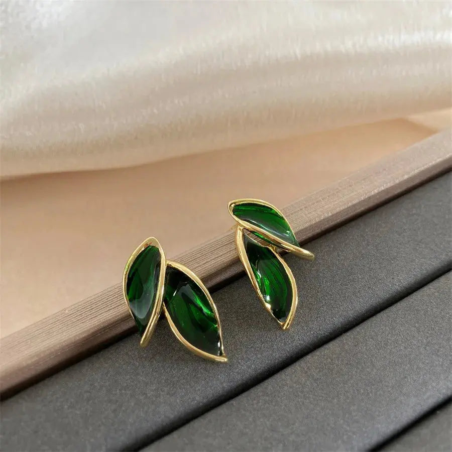 Gold earrings with green gemstones on a textured surface