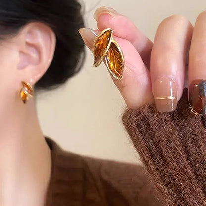 Close-up of a person wearing gold leaf-shaped earrings with a blurred background.