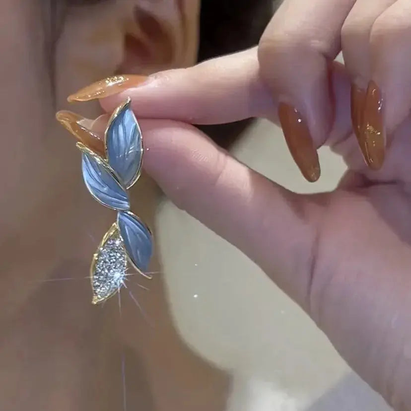 Close-up of a hand holding a decorative earring with leaf design.