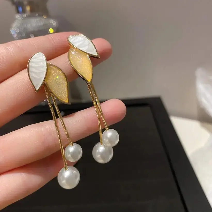 Earrings with leaf-shaped pendants and pearl drops held by a hand against a neutral background.