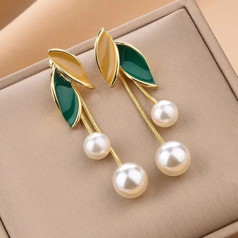 Pearl earrings with green leaf-like designs on a beige jewelry box