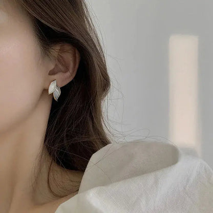 Close-up of a person wearing a silver leaf-shaped earring against a neutral background