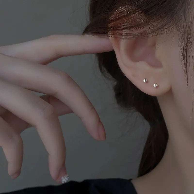 Close-up of a person wearing silver stud earrings with a neutral background