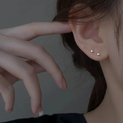 Close-up of a person wearing silver stud earrings with a neutral background